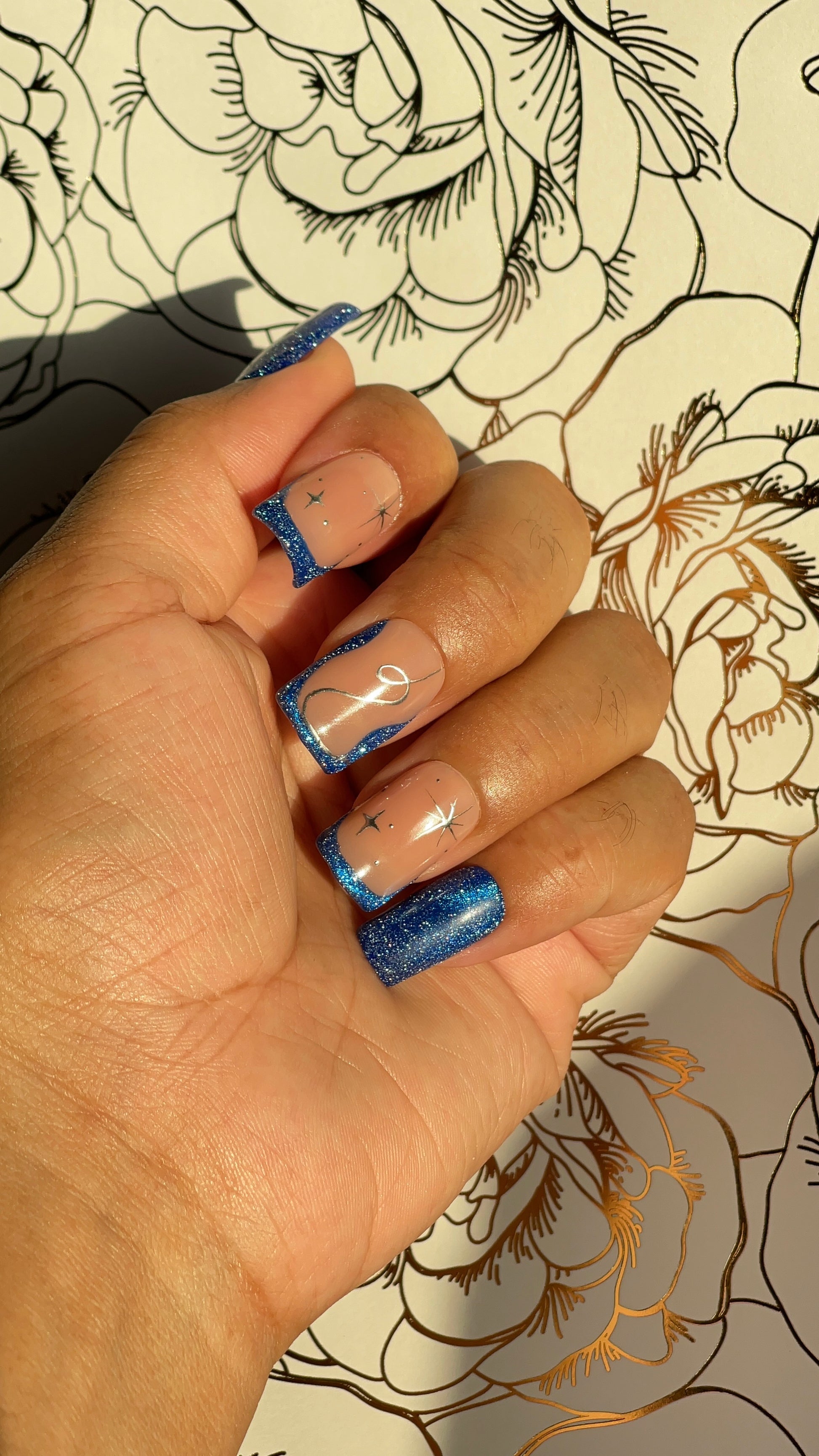 Blue galaxy glitter press-on nails with nude tones and silver constellations. A soft, celestial design inspired by deep winter nights.