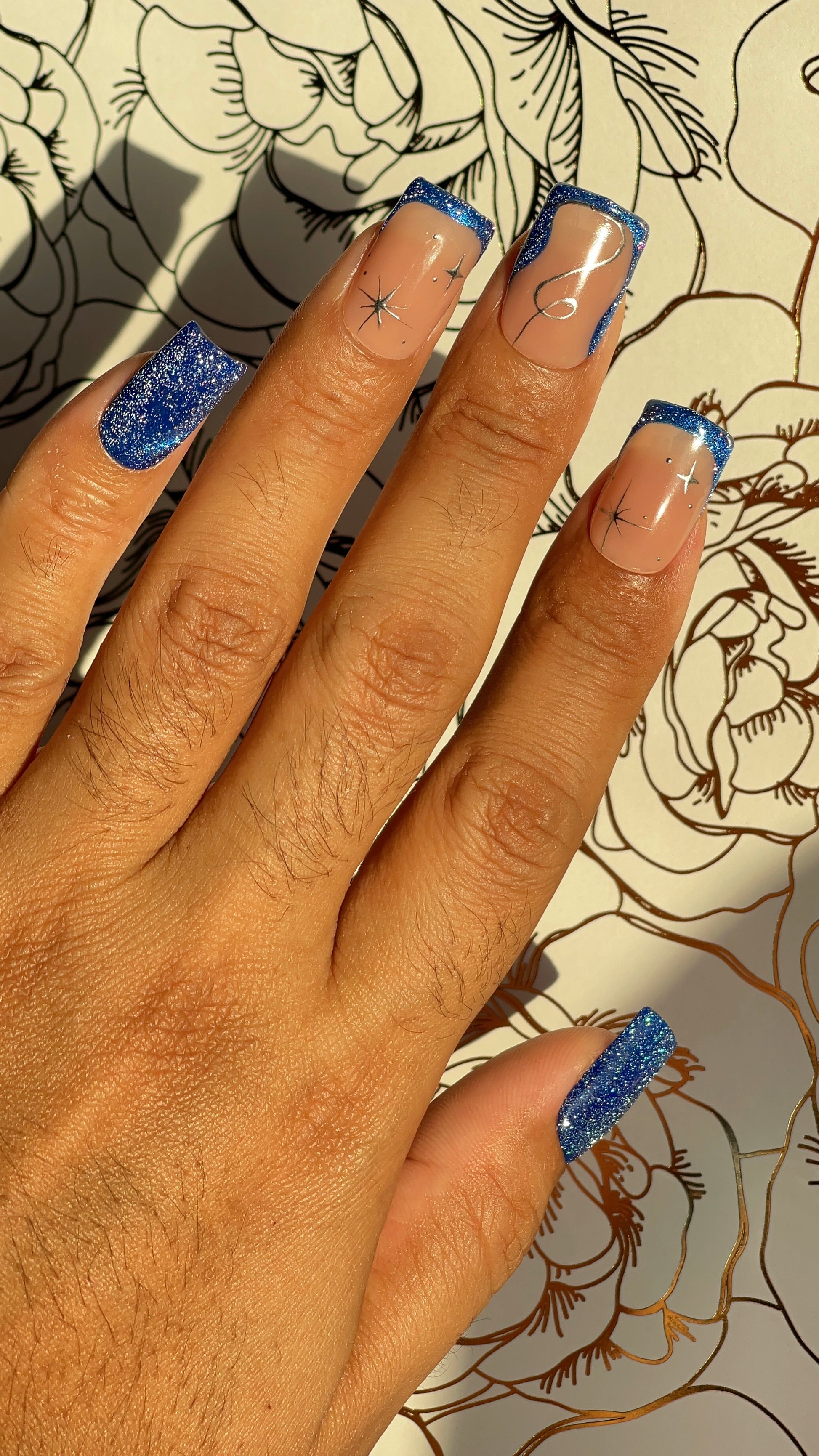 Blue galaxy glitter press-on nails with nude tones and silver constellations. A soft, celestial design inspired by deep winter nights.